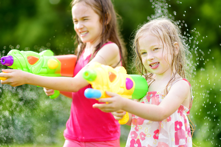 Adorable little girls playing with water guns on hot summer day. Cute children having fun with water outdoors. Funny summer games for kids.の写真素材