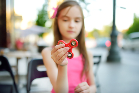 Cute school girl playing with colorful fidget spinner in outdoor cafe. Popular stress-relieving toy for school kids and adults.の写真素材