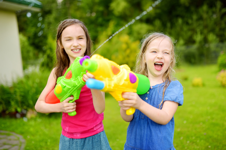 Adorable little girls playing with water guns on hot summer day. Cute children having fun with water outdoors. Funny summer games for kids.の写真素材