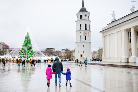Family of three enjoying their time by the Christmas tree in Vilnius, Lithuania. Celebrating Xmas holidays in Baltic states. Traveling in winter.の写真素材