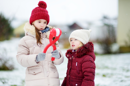 Two adorable little girls having fun with snowball maker in beautiful winter park. Beautiful sisters playing in a snow. Winter activities for kids.の写真素材