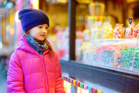Cute little girl choosing sweets on traditional Christmas market on chilly winter day. Kid buying candy and cookies on Xmas day.の写真素材