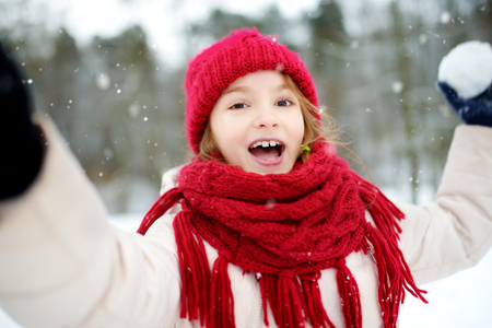 Adorable little girl having fun in beautiful winter park. Cute child playing in a snow. Winter activities for kids.の写真素材