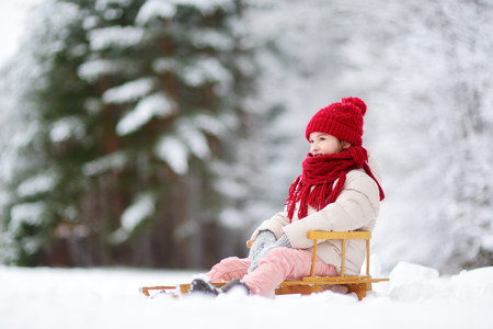 Funny little girl having fun with a sleight in beautiful winter park. Cute child playing in a snow....