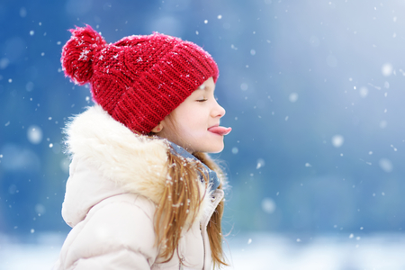 Adorable little girl catching snowflakes with her tongue in beautiful winter park. Cute child playing in a snow. Winter activities for kids.の写真素材