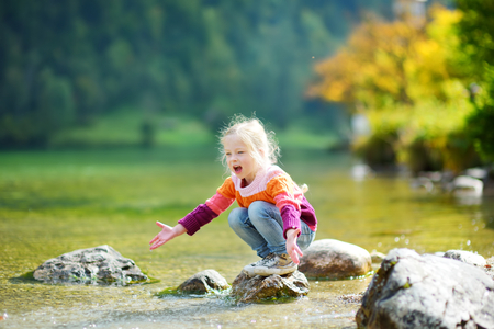 Adorable girl playing by Konigssee lake in Germany on warm summer day. Cute child having fun feeding ducks and throwing stones into the lake. Summer activities for kids.の写真素材
