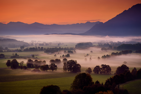 Breathtaking morning lansdcape of small bavarian village covered in fog. Scenic view of Bavarian Alps at sunrise with majestic mountains in the background, Anger, Germany.の写真素材