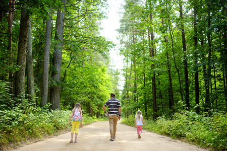 Two cute little sisters hiking in a forest with their father on beautiful summer day. Family time.の写真素材
