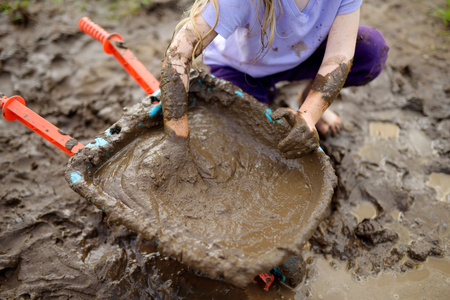 Funny little girl playing in a large wet mud puddle on sunny summer day. Child getting dirty while...