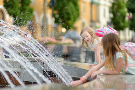 Two cute little girls playing by city fountain on hot and sunny summer day. Children having fun with water in summer. Active leisure for kids.の写真素材
