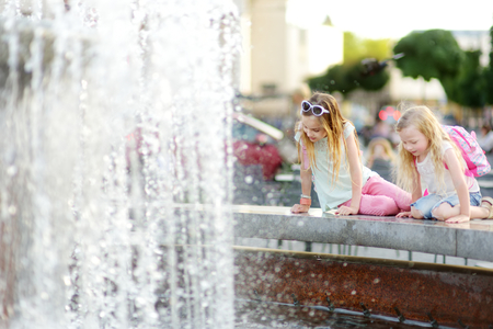Two cute little girls playing by city fountain on hot and sunny summer day. Children having fun with water in summer. Active leisure for kids.の写真素材