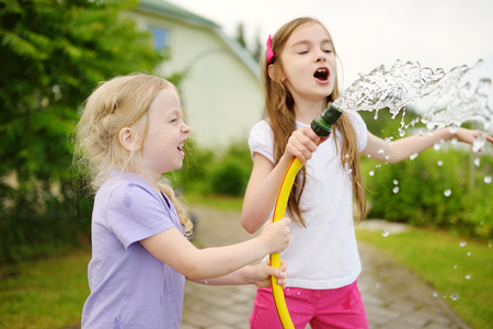 Adorable little girls playing with a garden hose on warm summer day. Outdoor activities for kids.の写真素材