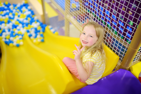 Happy little girl having fun in ball pit in kids indoor play center. Child playing with colorful balls in playground ball pool. Activity toys for little kids.の写真素材