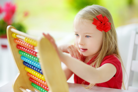 Cute little girl playing with wooden abacus at home. Smart child learning to count. Preschooler having fun with educational toy at home or kindergarten.の写真素材