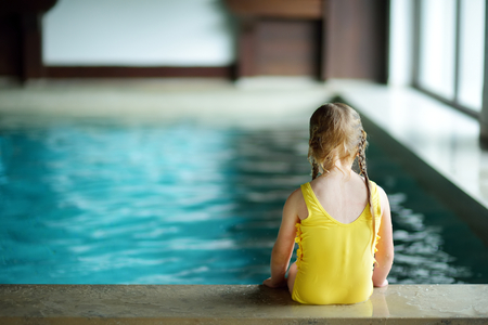Cute little girl playing with inflatable ring in indoor pool. Child learning to swim. Kid having fun with water toys. Family fun in a pool.の写真素材