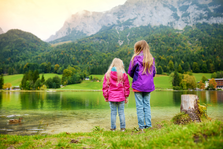 Two little girls enjoying the view of wonderful green waters of Hintersee lake. Amazing autumn landscape of Bavarian Alps on the Austrian border, Germany, Europe.の写真素材