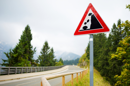 Falling rocks road sign on winding road in German Alps. Warning road sign in the mountains. Bavaria, Germany.の写真素材