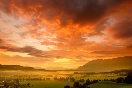 Breathtaking morning lansdcape of small bavarian village covered in fog. Scenic view of Bavarian Alps at sunrise with majestic mountains in the background, Anger, Germany.の写真素材