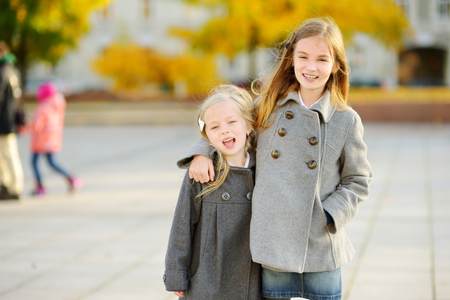 Two cute little girls having fun on beautiful autumn day. Happy children playing in autumn park. Kids gathering yellow fall foliage. Autumn activities for children.の写真素材