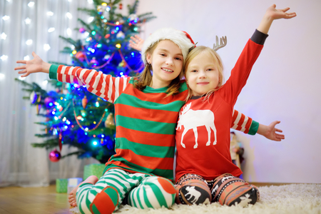 Two adorable sisters decorating a Christmas tree with colorful glass baubles at home. Family leisure at wonderful Xmas time. Trimming a festive tree.の写真素材