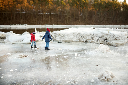 Two happy sisters playing with ice blocks by frozen river during an ice break. Children having fun in winter. Winter activities for kids.の写真素材