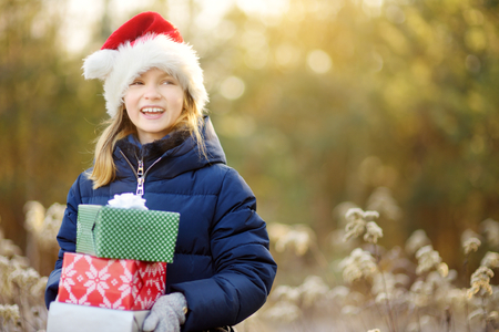 Adorable little girl holding a pile of Christmas gifts on beautiful sunny winter day. Celebrating Xmas at home.の写真素材