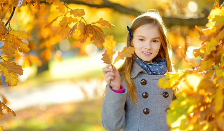Cute little girl having fun on beautiful autumn day. Happy child playing in autumn park. Kid gathering yellow fall foliage. Autumn activities for children.の写真素材