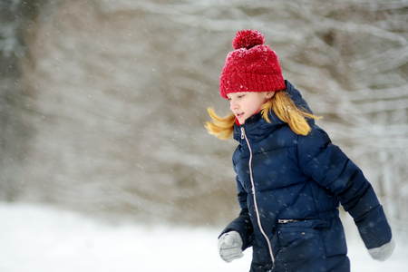 Adorable little girl having fun in beautiful winter park. Cute child playing in a snow. Winter activities for kidsの写真素材