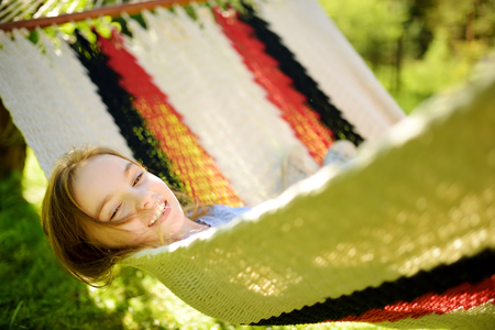 Happy little girl relaxing in hammock on beautiful summer day. Cute child having fun in spring garden. Family leisure at summer.の写真素材