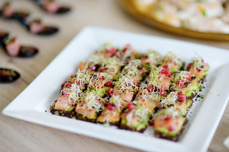 Delicious smoked salmon and avocado mini snacks served on a party or wedding reception. Plates with...