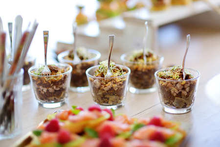 Fresh and delicious vegetable and pork salad served in mini glasses on a party or wedding reception. Plates with assorted fancy finger food snacks on an event party or dinner.の写真素材