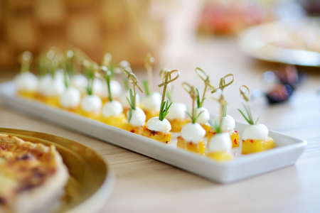 Delicious baked pineapple and mozzarella mini snacks served on a party or wedding reception. Plates with assorted fancy finger food snacks on an event party or dinner.の写真素材