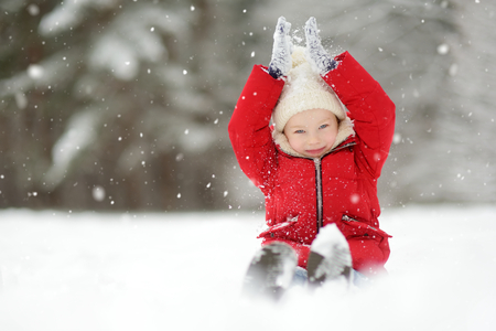 Adorable little girl having fun in beautiful winter park. Cute child playing in a snow. Winter activities for kidsの写真素材