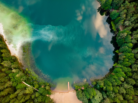 Aerial top down view of beautiful green waters of lake Gela. Birds eye view of scenic emerald lake surrounded by pine forests. Clouds reflecting in Gela lake, near Vilnius city, Lithuania.の写真素材