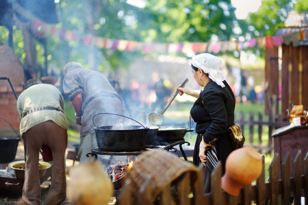 TRAKAI, LITHUANIA - JUNE 16, 2018: Historical reenactment activists preparing food over an open fire during annual Medieval Festival, held in Trakai Peninsular Castle. Recreating medieval town spirit.のeditorial素材