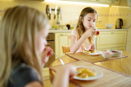 Cute little sisters enjoying their breakfast at home. Pretty children eating pancakes with strawberry sauce before school. Healthy nutrition for children.の写真素材