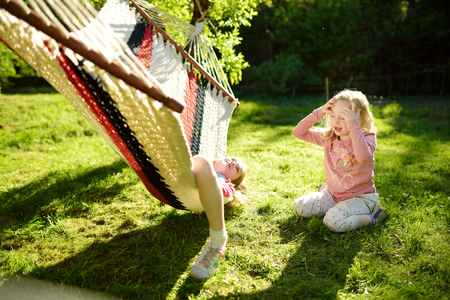 Cute little sisters having fun in hammock on beautiful summer day. Children relaxing in spring garden. Family leisure at summer.の写真素材