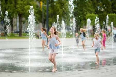 Cute young sisters playing in fountains on newly renovated Lukiskes Square in Vilnius, Lithuania. Children having fun with water on sunny summer day. Active leisure for kids.の写真素材