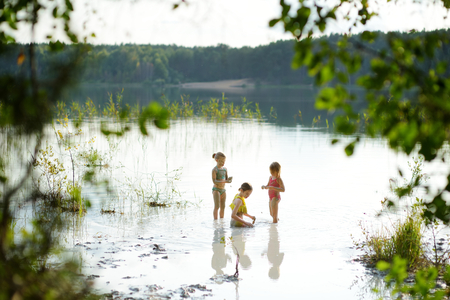 Three young sisters taking healing mud baths on lake Gela near Vilnius, Lithuania. Children having fun with mud. Kids playing with medicinal clay.の写真素材