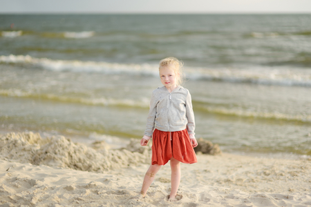 Cute little girl having fun on a sandy beach on warm and sunny summer day by the sea. Kid playing by the ocean. Summer activities for children.の写真素材