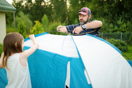 Cute little girls helping their parent to set up a tent on a campsite. Active lifestyle, family recreational weekend, summer outdoor.の写真素材