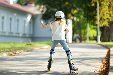 Pretty young girl learning to roller skate on beautiful summer day in a park. Child wearing safety helmet enjoying roller skating ride outdoors.の写真素材