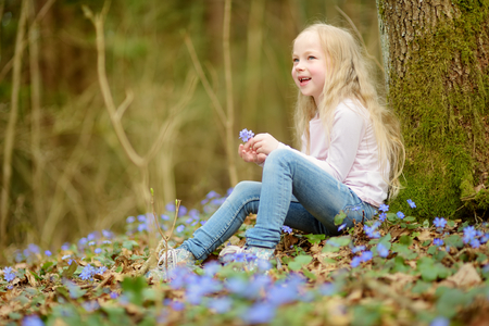 Adorable little girl picking the first flowers of spring in the woods on beautiful sunny spring day. Cute child having fun outdoors.の写真素材