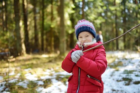 Cute young girl having fun during forest hike on beautiful winter day. Active family leisure with kids. Family fun.の写真素材