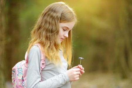 Adorable little girl picking the first flowers of spring in the woods on beautiful sunny spring day. Cute child having fun outdoors.の写真素材