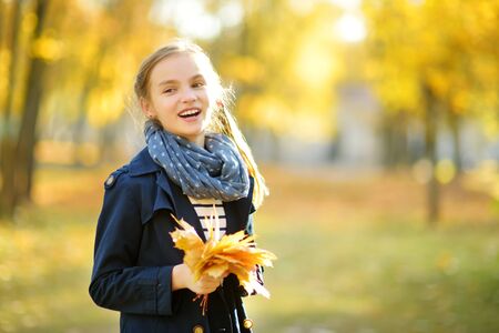 Adorable young girl having fun on beautiful autumn day. Happy child playing in autumn park. Kid gathering yellow fall foliage. Autumn activities for children.の写真素材