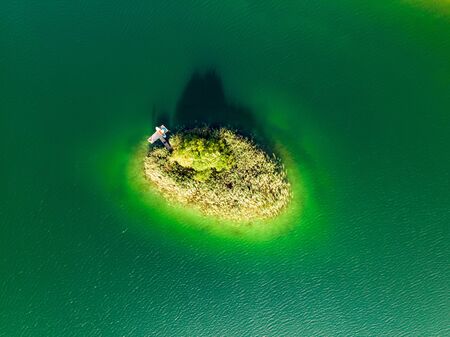 Aerial top down view of a small island. Birds eye view of beautiful green waters of lake Gela surrounded by pine forests. Clouds reflecting in Gela lake, near Vilnius city, Lithuania.の写真素材