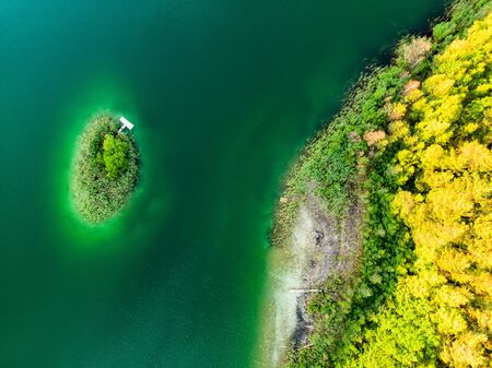 Aerial top down view of a small island. Birds eye view of beautiful green waters of lake Gela surrounded by pine forests. Clouds reflecting in Gela lake, near Vilnius city, Lithuania.の写真素材