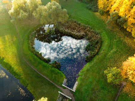 Birds eye view of autumn forest and a small lake. Aerial colorful forest scene in autumn with orange and yellow foliage. Fall scenery in Vilnius, Lithuania.の写真素材