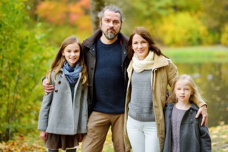Young family of four having fun in autumn park. Parents and two kids enjoying themselves on warm...